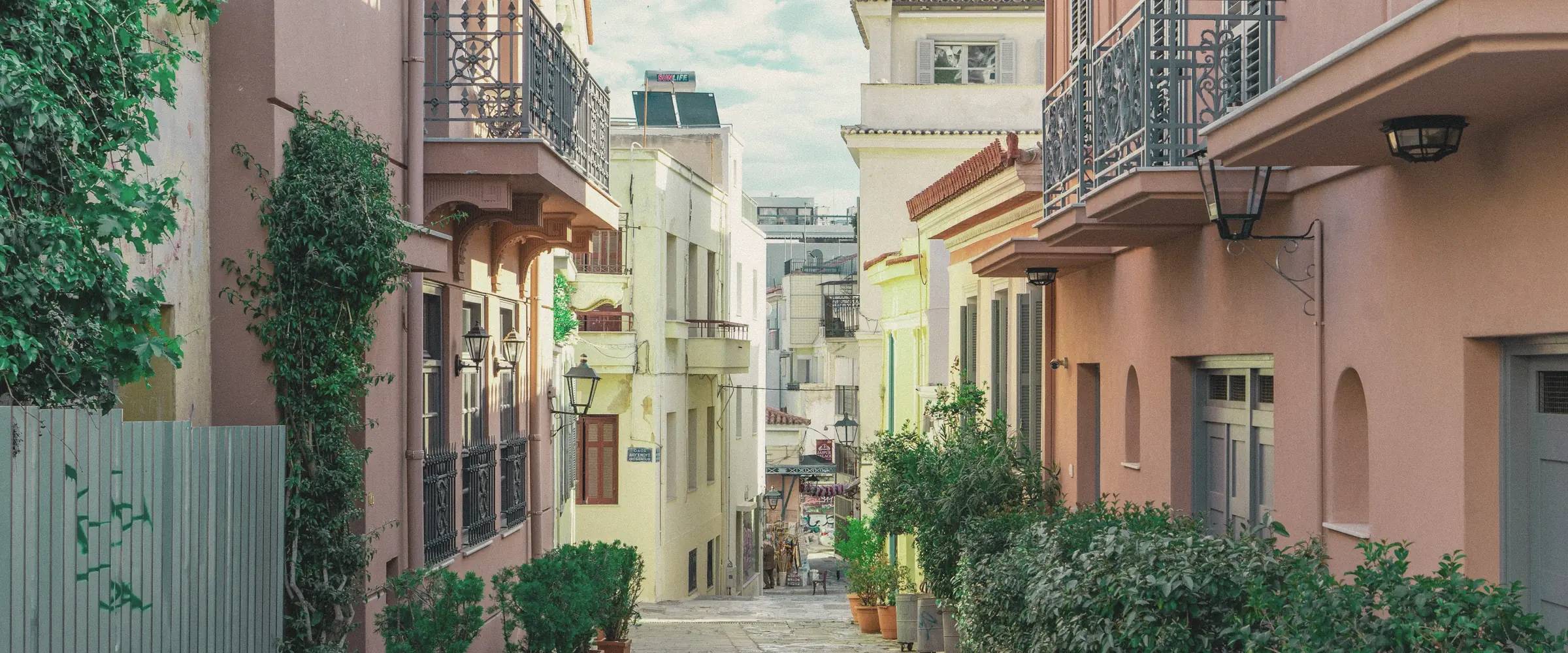 A narrow lane in Athens' old Plaka quarter lined with potted plants and pastel houses.