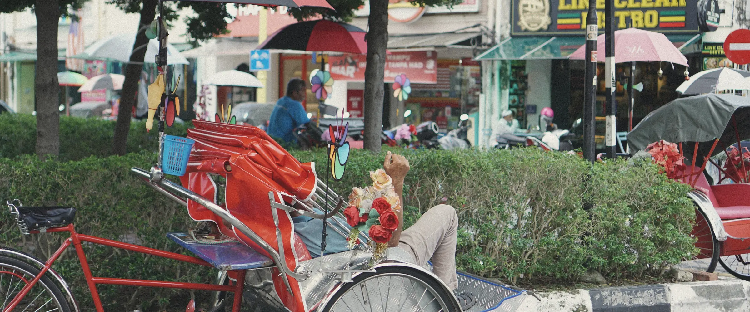 A trishaw driver rests beneath colourful umbrellas on a street in George Town, Penang.