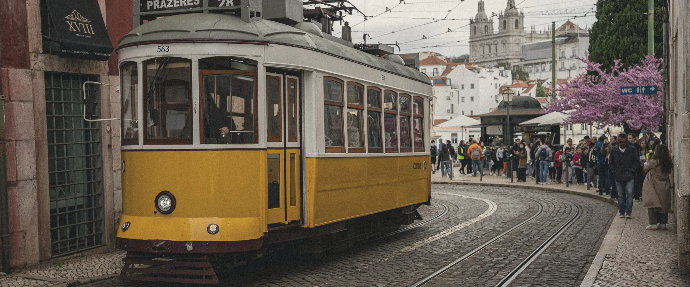 A yellow tram climbs a cobbled street between old Lisbon buildings.